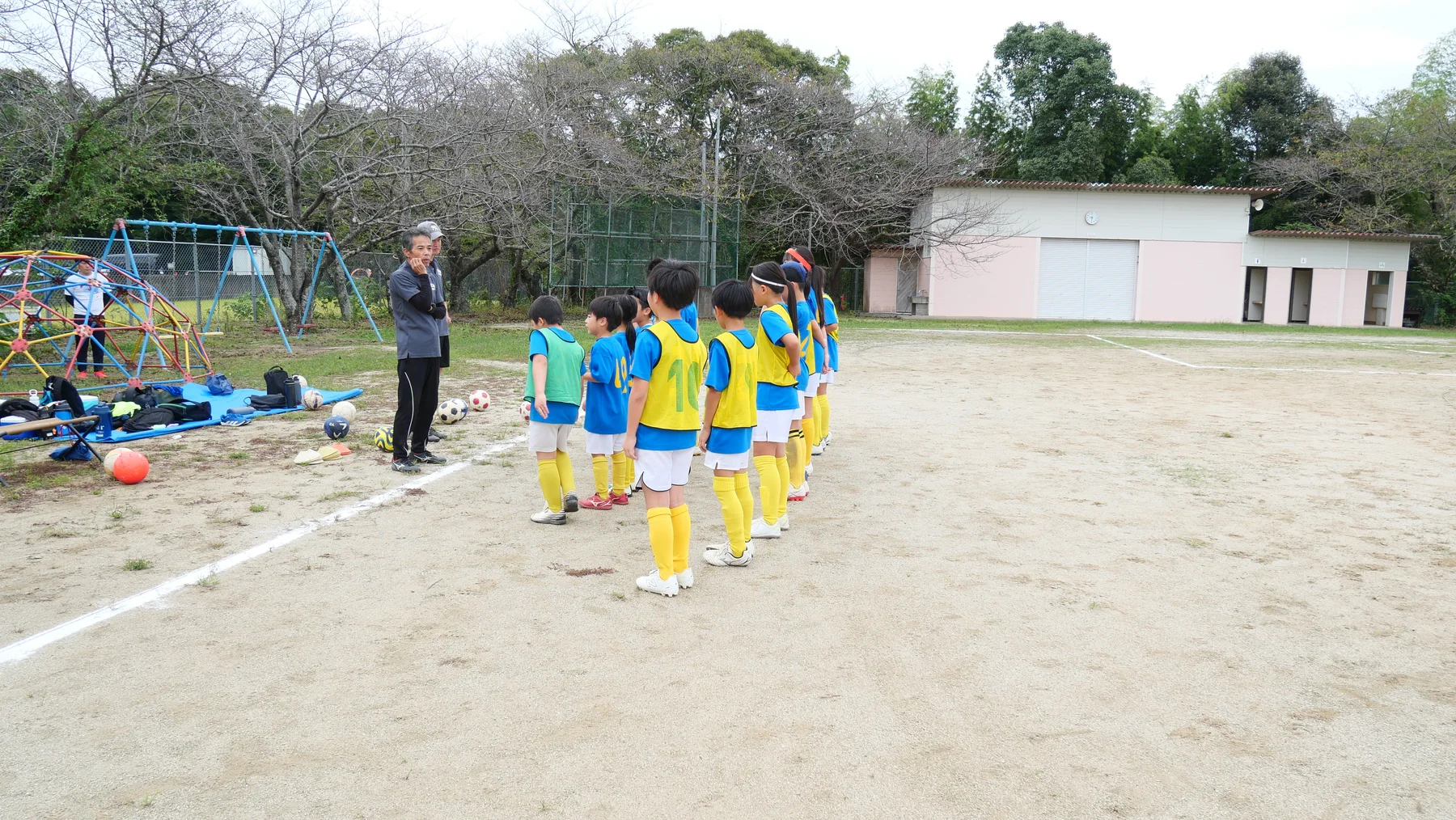 三並小学校のグラウンドでコーチの話を聞くFC朝倉の選手たち